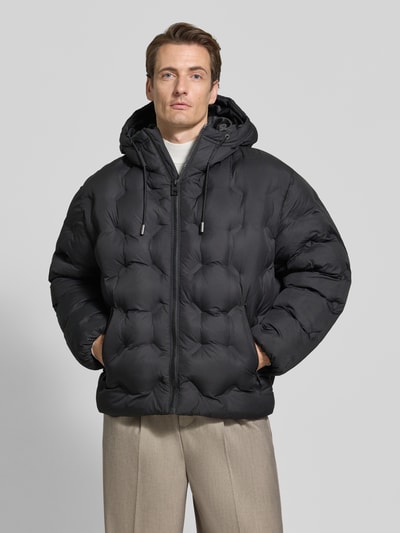 Männermodel trägt Regular Fit Steppjacke mit Rumftunnelzug Modell 'Barbo2641' von HUGO, unifarben schwarz, Popeline, Ganzkörperansicht von vorne.