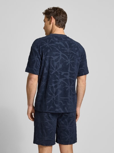 Männermodel trägt Regular Fit T-Shirt aus Baumwoll-Mix Modell 'TE_FLOWER' von BOSS Orange mit Allover-Muster in Dunkelblau, Frottee-Struktur, Ganzkörperansicht Rückansicht.
