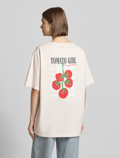 Frauenmodel trägt Oversized T-Shirt mit Label-Stitching von OH APRIL in Creme mit rotem Print, reine Baumwolle, Rückansicht, Ganzkörperansicht.
