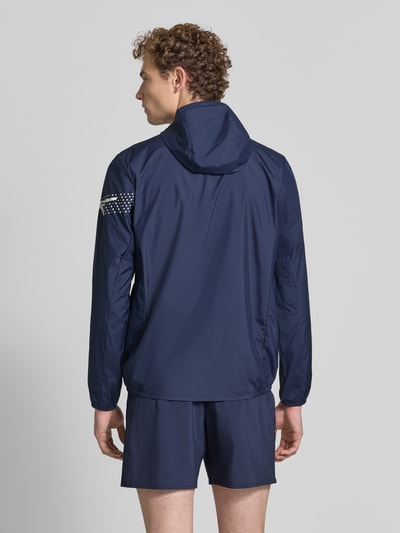 Männermodel trägt Regular Fit Jacke mit Logo-Print Modell 'ICON' von ASICS TIGER, dunkelblau, glatter Stoff, Ganzkörperansicht Rückansicht, krój regular fit, nadruk z logo, Model 'ICON', Kaptur ze stójką, zamek błyskawiczny, elastyczne wykończenia, Długość tyłu w rozmiarze M: 72 cm, Długość rękawów w rozmiarze M: 67 cm