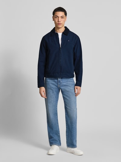 Männermodel trägt Regular Fit Blouson aus reiner Baumwolle von Tommy Jeans, dunkelblau, unifarben, Reißverschluss, Ganzkörperansicht von vorne.