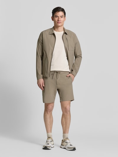 Männermodel trägt Straight Fit Shorts mit Eingrifftaschen Modell 'Drift' von SCANDINAVIAN EDITION in Beige, Ganzkörperansicht von vorne.