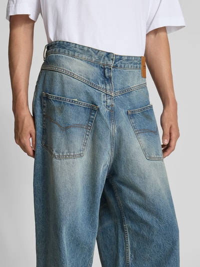 Männermodel trägt Loose Fit Jeans aus Baumwolle von VETEMENTS im Destroyed-Look, 5-Pocket-Design, mittleres Blau, Ganzkörperansicht Rückansicht.