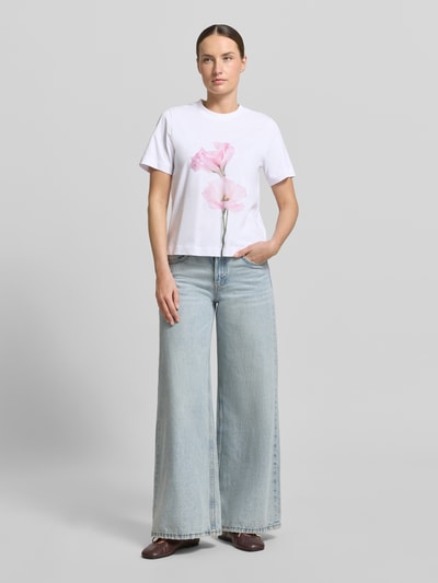 Frauenmodel trägt T-Shirt mit Motiv-Print Modell 'FIORE' von Stefanel, reine Baumwolle, Weiß mit rosa Blume, gerader Schnitt, Ganzkörperansicht von vorne.