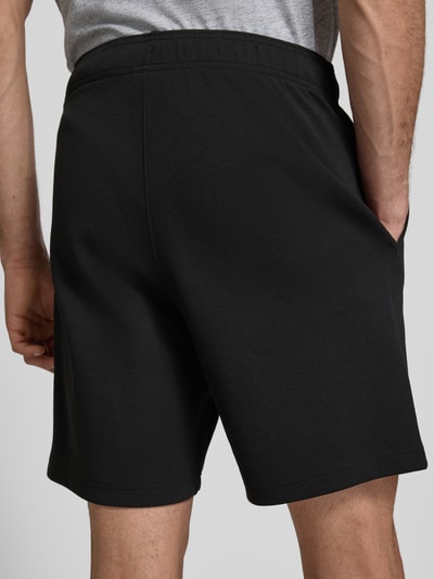 Männermodel trägt Shorts mit elastischem Bund und Label-Stitching von CHAMPION aus schwarzem Baumwoll-Mix, Ganzkörperansicht Rückansicht.