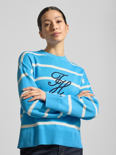 Frauenmodel trägt Regular Fit Sweatshirt aus reiner Baumwolle von Tommy Hilfiger, Optik:Allover-Muster, gestreift, Logo-Stitching, Kragenform Crew Neck, Rundhals, Ärmelform Langarm, Ärmelabschluss gerippt, Rumpfabschluss gerippt, Materialverarbeitung Feinstrick, Material: reine Baumwolle, Blautöne mit weißen und beigefarbenen Streifen, feine Stricktextur, Nahaufnahme Oberkörper.