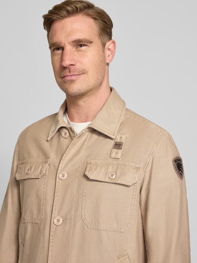 Męski model nosi Regular Fit Hemdjacke mit Brusttaschen Modell 'Goodale' od Blauer Usa, beżowa bawełna, widok z przodu, zbliżenie na górną część ciała. Szerokość w rozmiarze M: 55 cm, długość tyłu: 72 cm, szerokość ramion: 52 cm, długość rękawa: 68 cm.