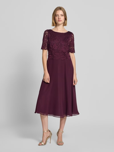 Frauenmodel trägt Tailliertes Cocktailkleid mit Spitzenbesatz von Vera Mont in Dunkelviolett, fließender Stoff, Spitzendetails, Ganzkörperansicht von vorne.