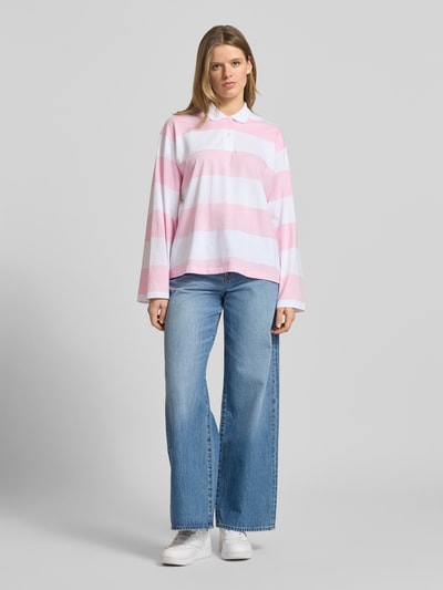 Frauenmodel trägt Relaxed Fit Poloshirt aus reiner Baumwolle Modell 'VILMA' von JJXX, rosa-weiß gestreift, Jeans, Ganzkörperansicht von vorne.
