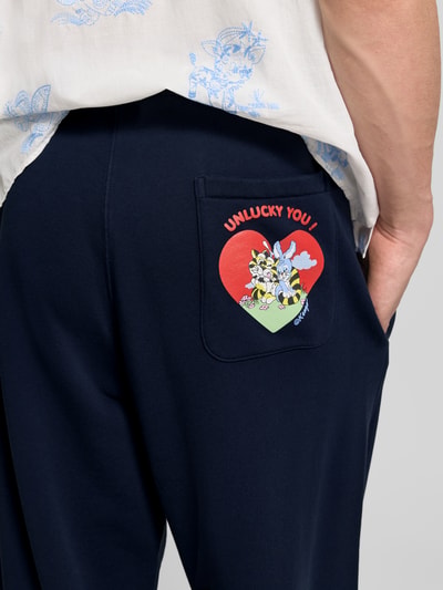 Männermodel trägt Wide Fit Sweatpants mit Eingrifftaschen von Kenzo aus reiner Baumwolle, Gesäßtasche mit buntem Druck, Detailaufnahme Rückansicht.