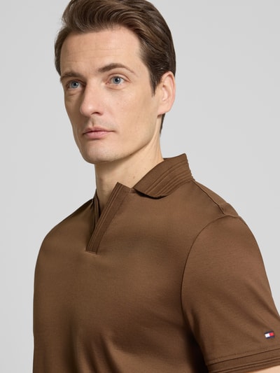 Männermodel trägt Regular Fit Poloshirt aus reiner Baumwolle von Tommy Hilfiger in Braun, unifarben, Logo-Detail, Nahaufnahme Oberkörper.