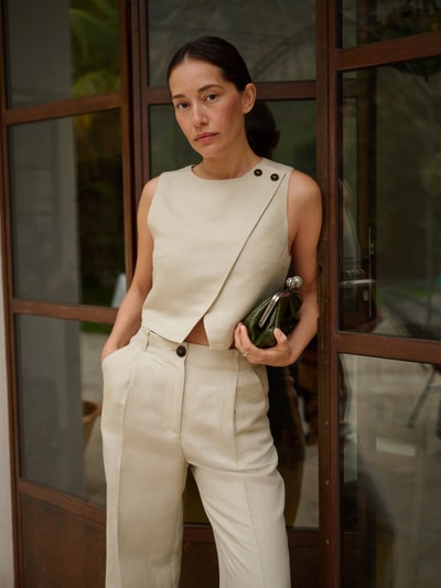 Frauenmodel trägt Cropped Bluse mit Knopfverschluss curated by Anna Schürrle von Style Icon Collection, Leinen-Viskose-Mix, helle Beige-Töne, glatte Textur, gerader Schnitt, Rundhalsausschnitt, Vorderansicht, Nahaufnahme Oberkörper.