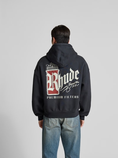 Männermodel trägt Oversized Sweatjacke aus Baumwolle von RHUDE in Dunkelblau mit großem Logo-Print, Rückenlänge 65 cm, Ganzkörperansicht Rückansicht.