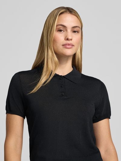 Frauenmodel trägt Poloshirt aus Viskose-Mix Modell 'LUXEN' von MANGO in Schwarz, taillierte Passform, Nahaufnahme Oberkörper.