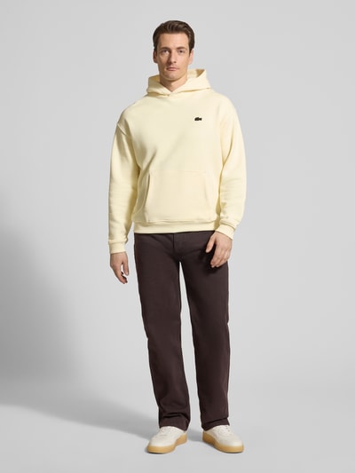 Męski model nosi Regular Fit Hoodie aus reiner Baumwolle von Lacoste, efekt: jednolity kolor, krój regular fit, naszywka z logo, nadruk z motywem, kaptur, długi rękaw, zakończenie rękawów i dołu prążkowane, kieszeń kangurka, wykończenie: dzianina dresowa, materiał: bawełna, całkowity widok z przodu.