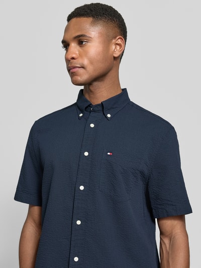Männermodel trägt Regular Fit Freizeithemd aus reiner Baumwolle von Tommy Hilfiger in Dunkelblau mit Brusttasche, Nahaufnahme Oberkörper.