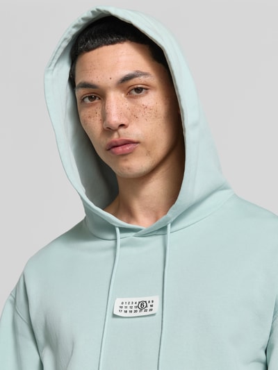 Männermodel trägt Regular Fit Hoodie mit Logo-Detail von MM6 Maison Margiela in Mint, reine Baumwolle, Nahaufnahme Oberkörper.