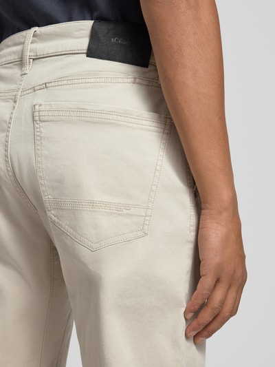 Mężczyznamodel nosi Regular Fit Chino aus Baumwoll-Mix von s.Oliver RED LABEL, jednolity beżowy kolor, bawełniany materiał, krój regular fit, widoczna tylna kieszeń, detal w postaci label patch, widok z tyłu, zbliżenie na górną część spodni.