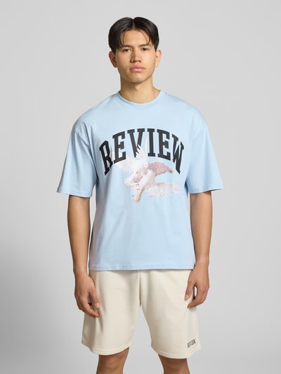 Mężczyzna nosi T-Shirt mit Logo- und Motiv-Print od REVIEW w jasnoniebieskim kolorze, z bawełny, krój loose fit, przód, ujęcie całej sylwetki.
