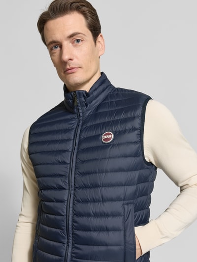 Męski model nosi Daunenweste mit Zweiwege-Reißverschluss von Colmar Originals, granatowy kolor, wypełnienie puchem i pierzem, krój regular fit, stójka, detal z logo, zamek błyskawiczny dwustronny, długość tyłu w rozmiarze 50: 62 cm, szerokość ramion w rozmiarze 50: 43 cm, szerokość w rozmiarze 50: 54 cm, ujęcie: zbliżenie górnej części ciała