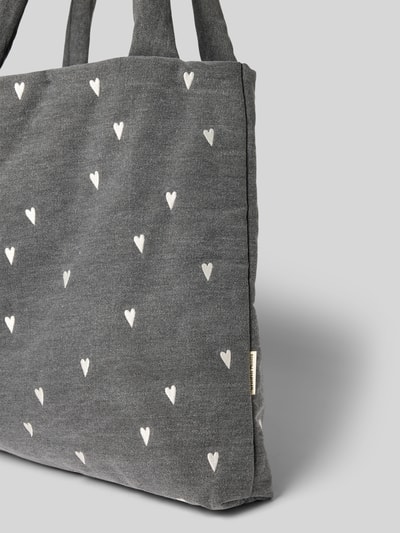Produktfoto, Tote Bag mit Logo-Detail in Denim-Optik von Studio Noos, grauer Stoff mit weißen Herz-Stickereien, strukturierte Textur, Trageriemen, Label-Detail, Allover-Motiv, rechteckige Form, dezentes Branding, Hauptfach mit Reißverschluss, modernes Accessoire für Damen.