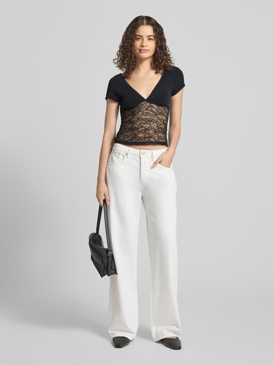Frauenmodel trägt Damen T-Shirt mit V-Ausschnitt und Spitze von Gina Tricot, Material-Mix mit Stretch-Anteil, Slim-Fit, Rückenlänge 51 cm, Schwarz mit transparenter Spitze, Ganzkörperansicht von vorne.