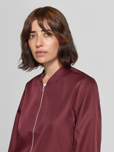 Frauenmodel trägt Bomberjacke mit Eingrifftaschen Modell 'PAPAYA' von VILA in dunklem Rot, glatte Textur, Nahaufnahme Oberkörper, Regular Fit, Stehkragen, Reißverschluss, Damenjacke.