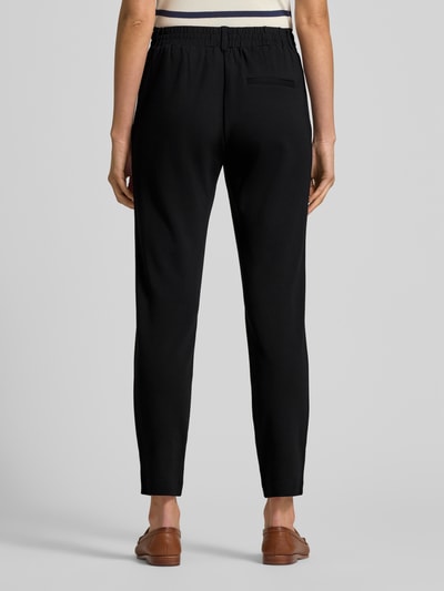 Kobieta prezentuje Easy Pants mit Bundfalten od TOM TAILOR, czarne, mieszanka wiskozy z dodatkiem streczu, zwężane nogawki, elastyczny pas, tunel, zakładki w pasie, wpuszczane kieszenie, ozdobna wypustka z tyłu, widok całej sylwetki od tyłu.
