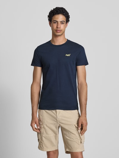 Männermodel trägt Regular Fit T-Shirt mit Logo-Stitching von Superdry, reine Baumwolle, dunkelblau, Rundhalsausschnitt, Ganzkörperansicht von vorne.