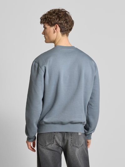 Männermodel trägt Sweatshirt mit Label-Stitching von Carhartt Work In Progress, graublau, Baumwoll-Mix, lockere Passform, Ganzkörperansicht Rückansicht.