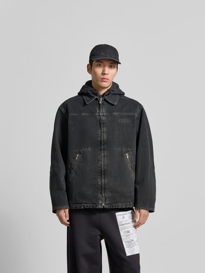 Männermodel trägt Jacke in Denim-Optik mit Umlegekragen von MM6 Maison Margiela in Schwarz, Relaxed Fit, Reißverschlusstaschen, Ganzkörperansicht von vorne