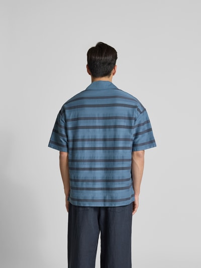 Männermodel trägt Oversized Poloshirt mit Logo-Patch von MAISON KITSUNÉ in Blau mit Streifen, Baumwolle, lockerer Schnitt, Ganzkörperansicht Rückansicht.
