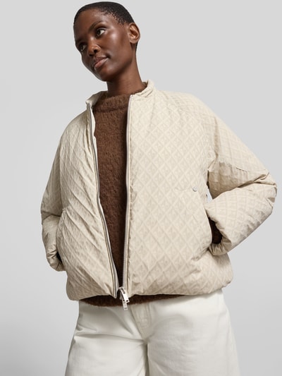Frauenmodel trägt Regular Fit Jacke mit Allover-Logo-Print von Moose Knuckles im Elastischer-Material-Mix, Zweiwege-Reißverschluss, cremefarbene geometrische Textur, Kapuze mit Tunnelzug, Rückenlänge 60 cm, Brustweite 59 cm, Ärmellänge 63 cm, Ganzkörperansicht von vorne.
