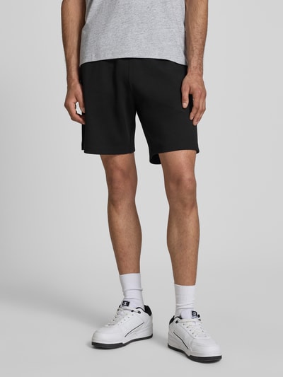 Männermodel trägt schwarze Shorts mit elastischem Bund und Label-Stitching von CHAMPION aus Baumwoll-Mix, Nahaufnahme Oberschenkel.