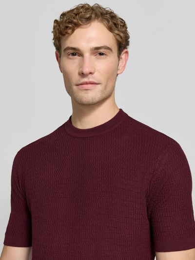 Männermodel trägt Slim Fit Strickshirt aus reiner Wolle von Emporio Armani in Dunkelrot mit gerippten Abschlüssen, Nahaufnahme Oberkörper.