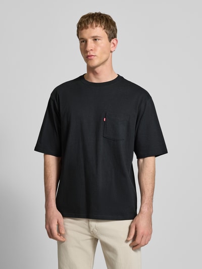 Männermodel trägt T-Shirt mit Brusttasche und Label-Detail von Levi's®, schwarze Reine Baumwolle, Gerader Schnitt, Ganzkörperansicht von vorne.