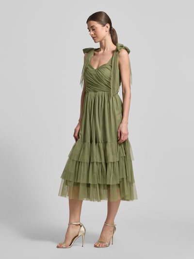Männermodel trägt Cocktailkleid aus Tüll im Stufen-Look von LACE & BEADS, linia a, sukienka midi, drapowania, długość tyłu w rozmiarze S: 103 cm, szerokość w rozmiarze S: 31 cm, kolor oliwkowy, tekstura tiulu i efekt stopniowania, Ganzkörperansicht von vorne.
