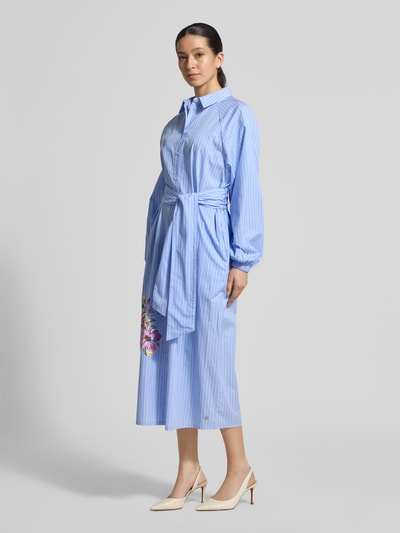 Vrouwenmodel draagt Regular Fit Maxikleid met floralem print van Fynch-Hatton in lichtblauw, puur katoen, bloemenprint, overhemdkraag, met lange mouwen, doorlopende knoopsluiting, elastische mouwboorden, getailleerde pasvorm, afneembaar stoffen band, ruglengte maat 36: 126 cm, borstwijdte maat 36: 57 cm, mouwlengte maat 36: 53 cm. Volledig lichaam van voren.