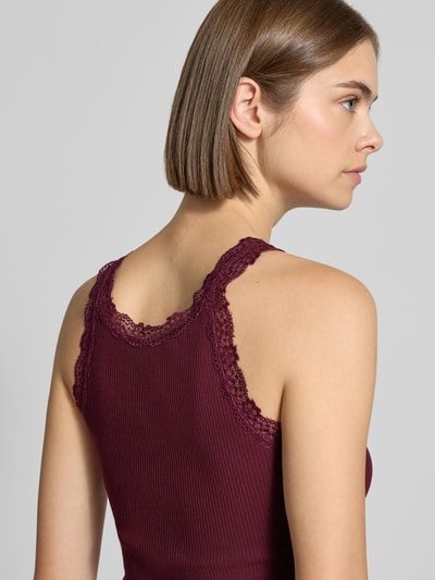 Kobiece model prezentuje top Slim Fit Tanktop aus Baumwoll-Mix model 'SARA SHARAI' od ONLY w kolorze bordowym z koronkowym wykończeniem, tekstura prążkowana, detailaufnahme ramion, damski top od ONLY