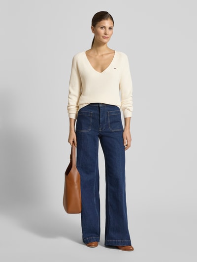 Vrouwenmodel draagt Regular Fit gebreide pullover uit puur katoen van Tommy Hilfiger met gestreepte look, gestikt logo, V-hals, lange raglanmouwen, ribtricot, effen kleur; Ganzkörperansicht von voren.
