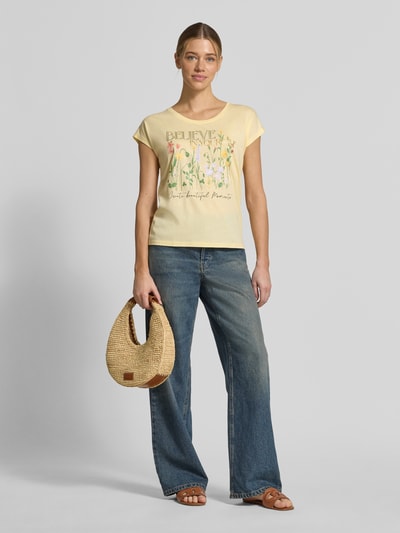 Kobiece model nosi T-Shirt mit Motiv-Print od Christian Berg Woman w jasnożółtym kolorze, krój regular fit, bawełna z wiskozą, okrągły dekolt, roślinny nadruk, długość tyłu w rozmiarze S: 54 cm, pełny widok z przodu.