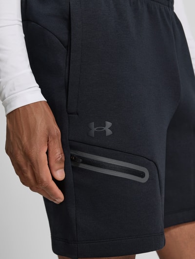 Mężczyznamodel nosi szorty z kieszenią zapinaną na zamek błyskawiczny od Under Armour, mieszanka bawełny, krój regular fit, logo, elastyczny pas, szerokość w rozmiarze M 39 cm, długość wewnętrzna nogawki w rozmiarze M 18 cm, zbliżenie na górną część nogi.