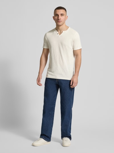 Männermodel trägt t-shirt uit puur katoen model 'SPLIT' van Jack & Jones, recht model, v-hals, knoopsluiting, ruglengte maat M 67 cm, lichte kleur, blauwe jeans, witte sneakers, ganzkörperansicht van voren