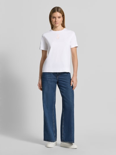 Frauenmodel trägt weißes T-Shirt mit Rundhalsausschnitt und Stitching Modell 'Tino' von JOOP!, reine Baumwolle, Regular Fit, kombiniert mit blauen Jeans, Ganzkörperansicht von vorne.
