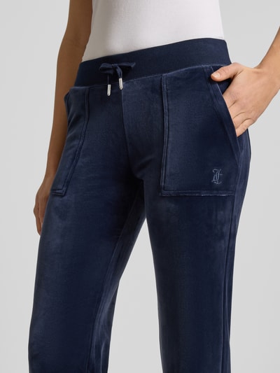 Frauenmodel trägt Low Rise Sweatpants mit elastischem Bund Modell 'LAYLA' von Juicy Couture aus dunkelblauem Baumwoll-Mix mit Stretch-Anteil, sichtbare Eingrifftaschen, Flared-Cut, Nahaufnahme Oberschenkel.