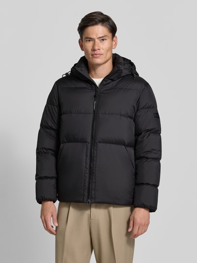 Männermodel trägt Regular Fit Daunenjacke mit Kapuzenkragen von Marc O'Polo in Schwarz, unifarben, wasserabweisend, Ganzkörperansicht von vorne.