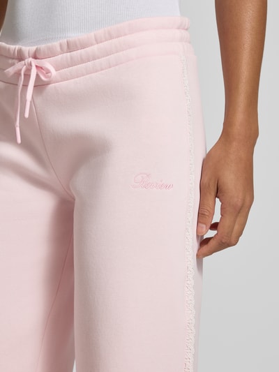 Frauenmodel trägt Wide Fit Sweatpants aus Baumwoll-Mix von REVIEW in Rosa mit Bordüre, Label-Stitching, Nahaufnahme Oberkörper.