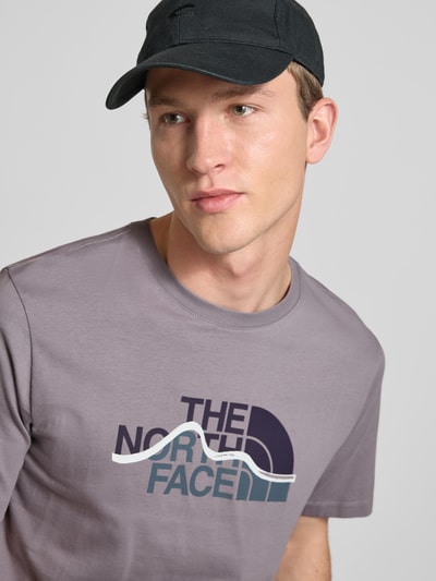 Männermodel trägt Regular Fit T-Shirt aus reiner Baumwolle Modell 'MOUNTAIN LINE' von The North Face in Grau mit Label-Print, Nahaufnahme Oberkörper. Herren T-Shirt, Rundhalsausschnitt, Rückenlänge bei Größe M 70 cm.