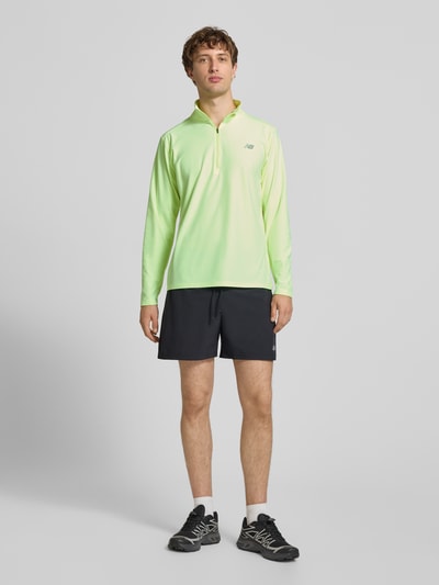 Mężczyzna model nosi Regular Fit Sweatshirt mit Troyer-Kragen od New Balance z elastyczną mieszanką materiałów i nadrukiem z logo, Długość tyłu w rozmiarze M: 69 cm, krój regular fit, jasna zieleń i gładka tekstura, Ganzkörperansicht von vorne.