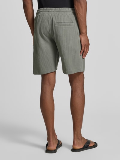 Männermodel trägt Shorts mit Strukturmuster Modell 'BRIKKO' von Drykorn aus Reine Baumwolle, Regular-Fit, elastischer Bund, Tunnelzug, Eingrifftaschen, Bundweite 39 cm, Innenbeinlänge 20 cm in Größe M, Ganzkörperansicht Rückansicht.